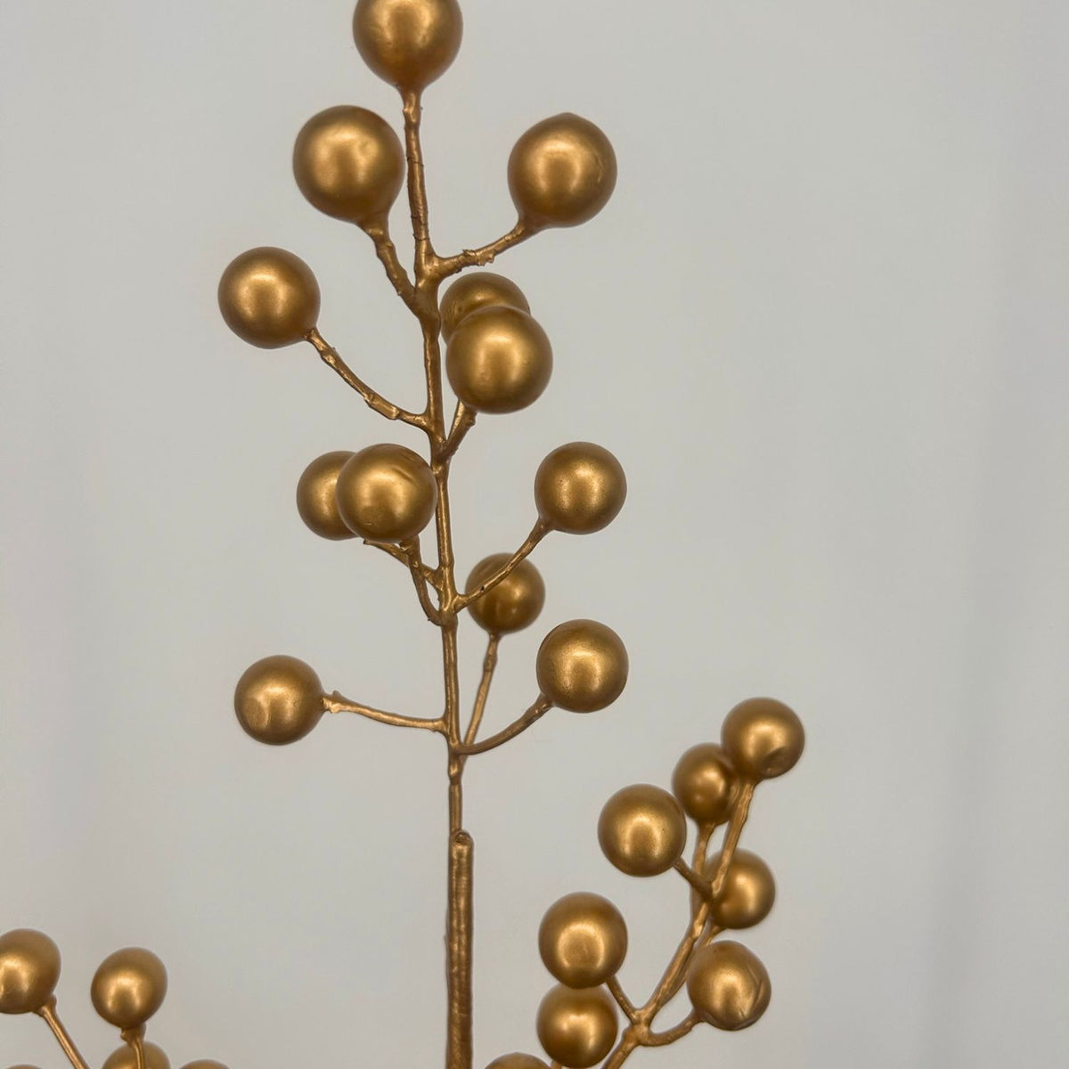 Gold artificial Christmas Berries against a grey background.