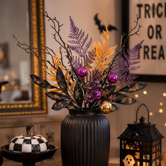 Halloween floral centerpiece in a ribbed black vase, featuring purple and gold faux foliage, black branches, glossy purple and gold ornaments, styled on a tabletop with a checkerboard pumpkin and a lantern in a warmly lit room.