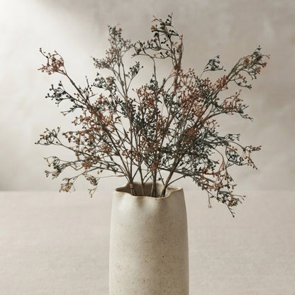 A beige ceramic vase holding a dried floral arrangement with delicate brown and gray stems, set against a soft neutral background.