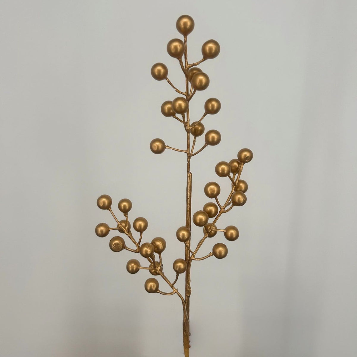 Gold artificial Christmas Berries against a grey background.