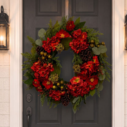 A festive artificial Christmas wreath hanging on a dark charcoal front door, decorated with vibrant red flowers, green foliage, pinecones, and small gold berries.