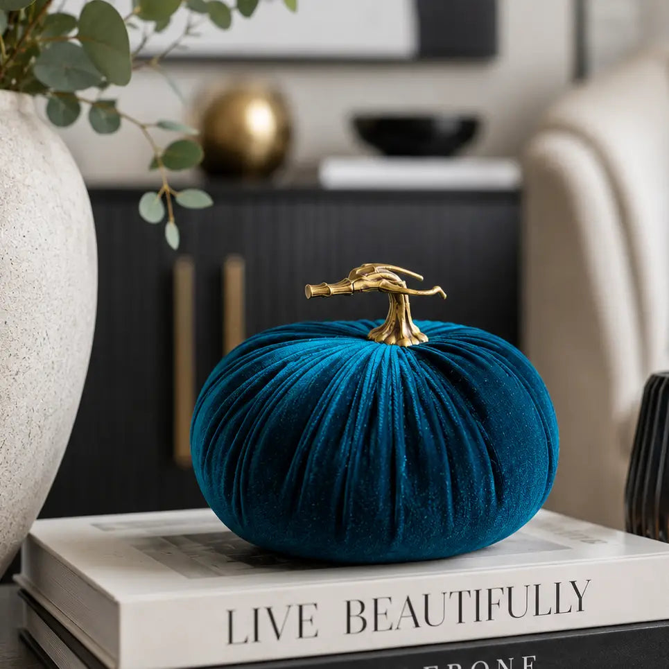 A teal velvet decorative pumpkin with a realistic stem sits on stacked books in a styled home interior setting.