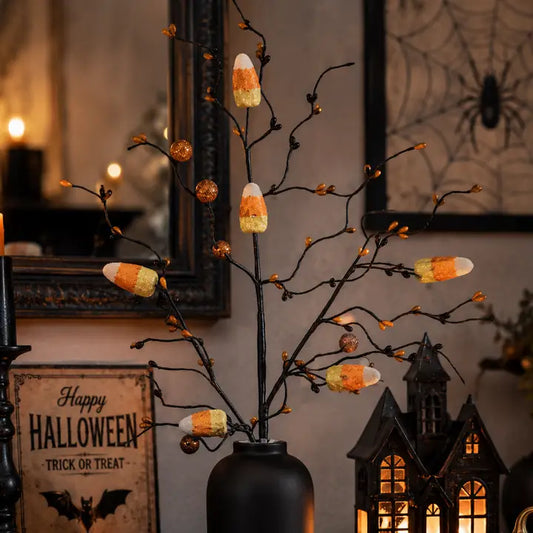 Halloween decorative branch arrangement with small orange jewels and candy corn accents in a black vase, styled in a cozy indoor setting with a Halloween sign and lantern in the background.